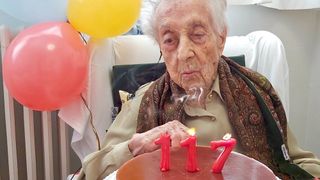 An elderly woman blows out candles on her birthday cake